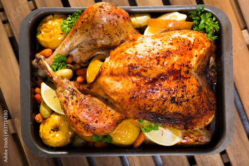 Tasty turkey baked with vegetables and apples, served with lemon slices and greens in baking dish