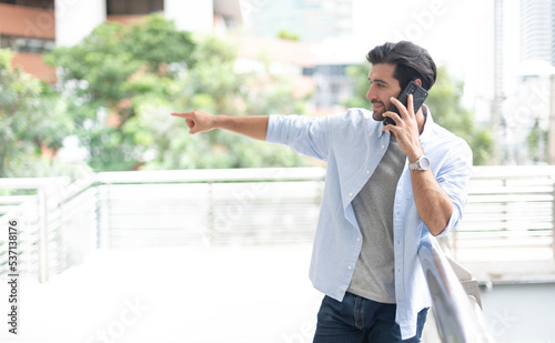 A businessman points to something while using a smartphone to talk with his friend outdoor.