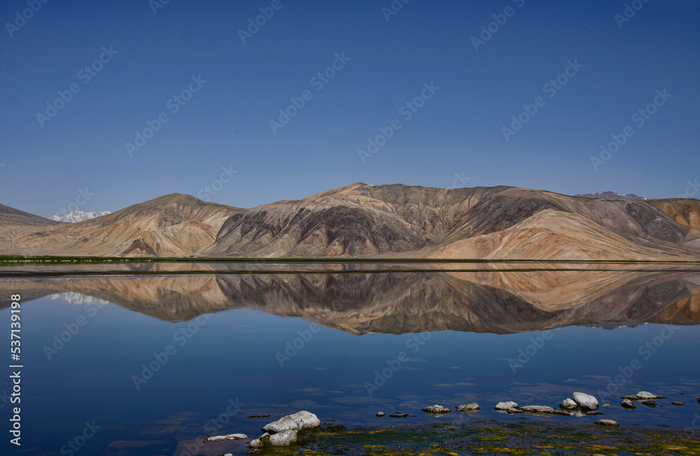 Reflecting rainbow mountains on Lake Bulunkul, Pamir Highway, Tajikistan