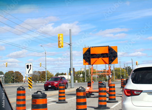 Road construction signs and pylons at intersection of busy road