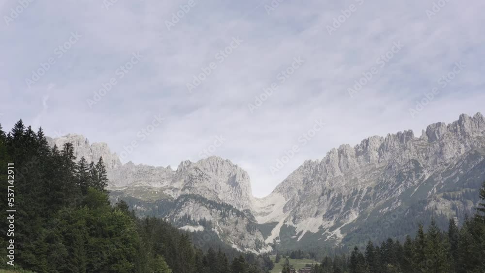Slow ascending drone shot of the famous Ellmauer Tor at the Wilde Kaiser, Tyrol. Low angle shot of dense forest along the foothills of a mountain range on a cloudy day in Austria, Europe. Slow ascending drone shot of the famous Ellmauer Tor at the Wilde Kaiser, Tyrol. Low angle shot of dense forest along the foothills of a mountain range on a cloudy day in Austria, Europe.