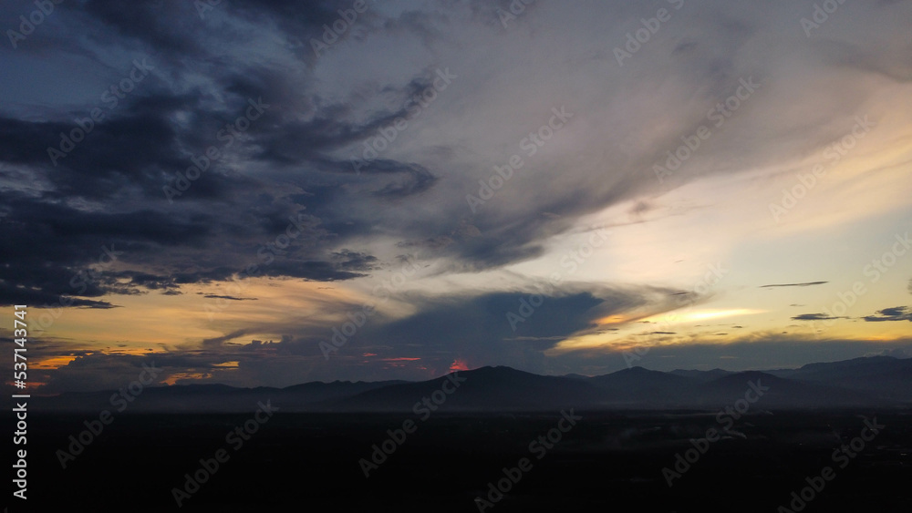 Aerial view of beautiful sky with clouds and sunlight during sunset. Time lapse of the clouds above the sky with the golden rays of the sun against the background of the silhouette of the mountain lan