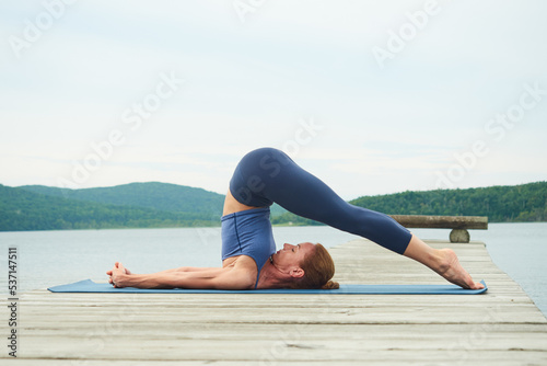Mature woman in blue sportswear practicing yoga against the backdrop of a seascape