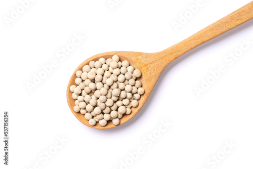 White pepper seeds (peppercorns) in wooden spoon isolated on white background, top view, flat lay.