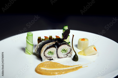 Fish fillet stuffed with cucumber. Rolled fish fillet in nori with vegetables on a black background. Asian seafood sushi. Side view photo