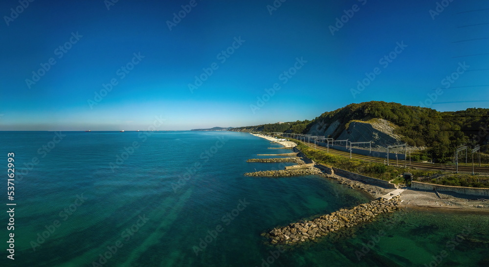 coast of the black sea with clear emerald water - stone breakwaters from boulders, seaside railway along the beach on a sunny  day