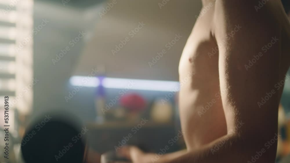Muscular young boy do dumbbells curls in his room. Closeup of his biceps and muscular abs. Checks his muscles in the mirror. Weight training, fitness, physical activity. Healthy lifestyle concept.