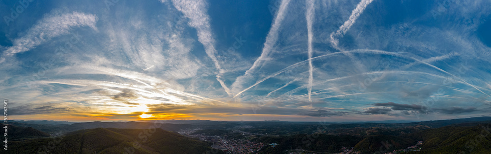 Aerial panorama view of colorful autumn sunset with visible airplane contrails, over Resita city, Romania. Captured from a drone.
