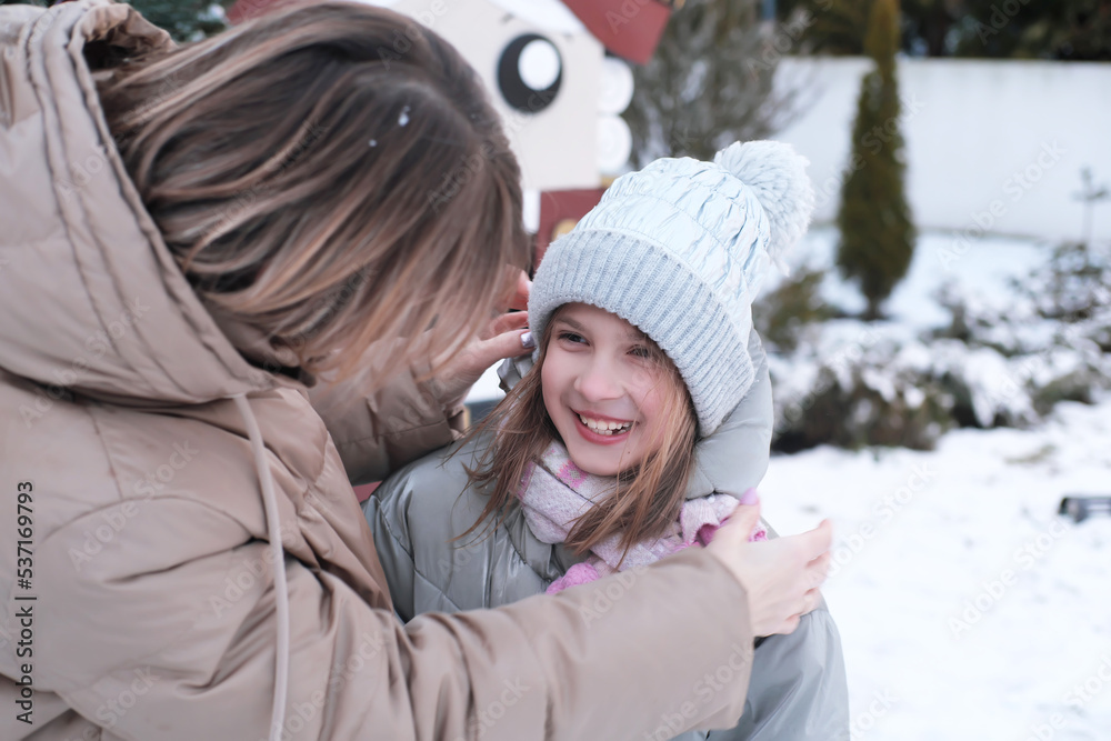 Mother puts on and adjusts the hat on her daughter on the street in winter