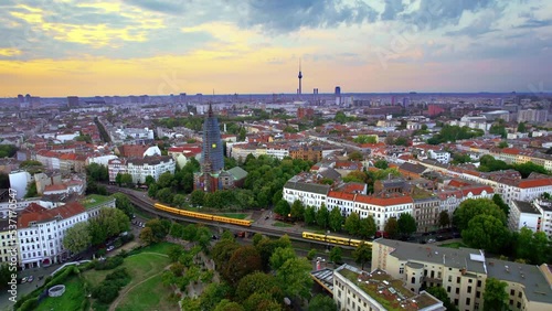 Aerial drone view of Kreuzberg, Berlin at sunset, Germany. Residential district with greenery, buildings and Berlin Television Tower in the distance, moving trains photo