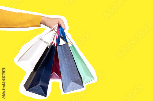 A hand holds paper bags for sale on a yellow background. Shopping concept. copy space