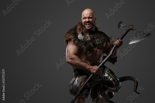 Portrait of furious nordic warrior with muscular build dressed in armor holding axe.