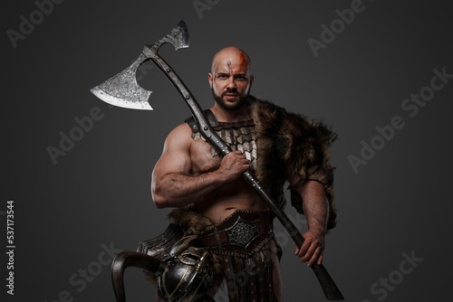 Shot of scandinavian barbarian with fur and horned helmet holding two handed axe.