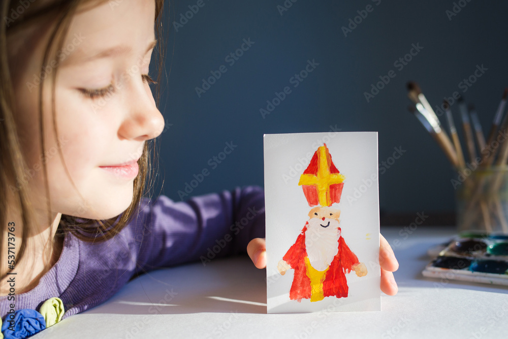 Φωτογραφία girl shows children's drawing - card for day of saint nicholas on table background for traditional Dutch holiday sinterklaas
