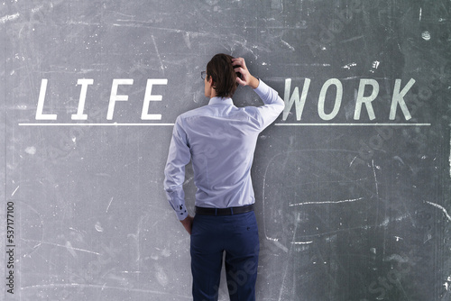 Attractive thoughtful young european businessman with writing on concrete wall trying to balance life and work. Success, career, failure, work, life and personal development concept.