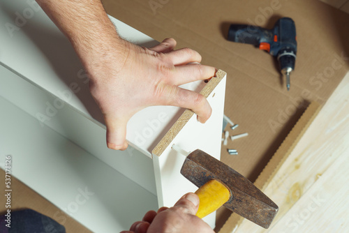 Wallpaper Mural Male hands hold metal hammer with yellow plastic handle, driving dowel, assembling white drawer of dresser or wardrobe. Self-assembly of furniture at home, DIY, furniture repair and rearrangement Torontodigital.ca