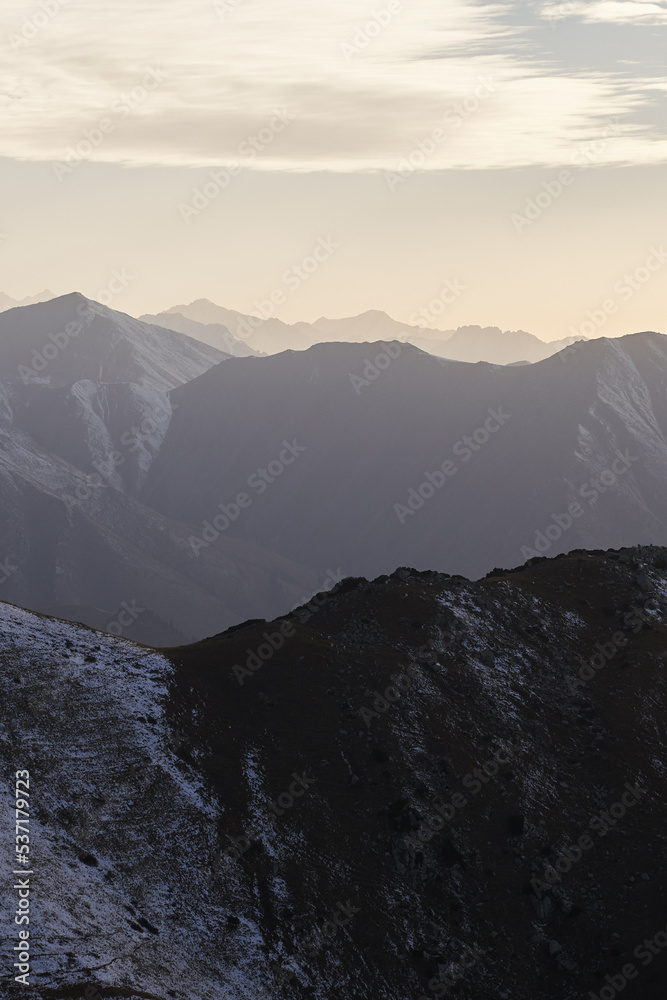 Vertical landscape with a view of mountain peaks with snow at sunset.