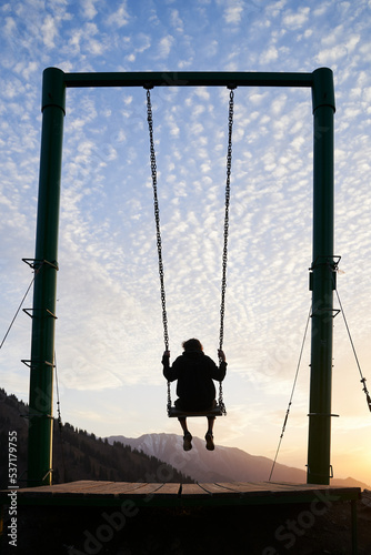 Young man is riding on a swing in mountains during a sunset.
