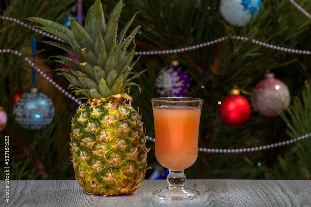 Pineapple, a glass of juice and a fir tree with Christmas ornaments. Pineapple, a glass of juice and a fir tree with Christmas ornaments.