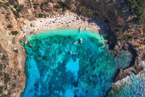 Top view of seascape with beautiful coastline and small sandy beach with colorful umbrellas. Sea coast with blue, turquoise clear water on a sunny day, aerial drone shot