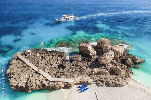 Aerial view beautiful seascape with stone dock and ship with tourists on sunny day top view. Sea coast with blue, turquoise clear water, aerial drone shot