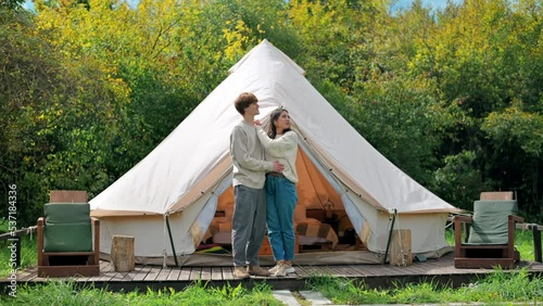 A couple hugging each other and talking on a tent terrace at glamping. Lush forest around