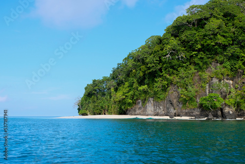 A steep high sided tropical island covered in trees and a pristine white sandy beach with turquoise green ocean water in remote Solomon Islands and Bougainville, Papua New Guinea 