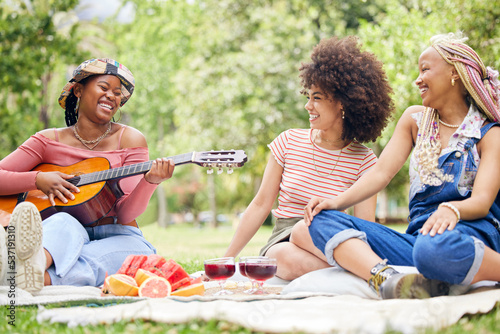 Girl friends, music and guitar at picnic with fruit, drinks and happy laughter in nature. Friendship, song and party on grass, group of black women having lunch together on blanket in park in Africa. © Wesley J/peopleimages.com