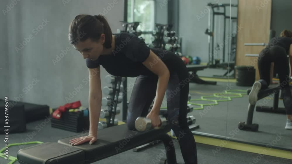 Young woman doing dumbbell row exercise on bench while training in gym