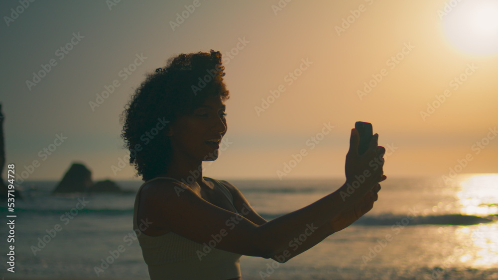 Girl smiling phone camera standing beach at sunrise closeup. Woman making selfie