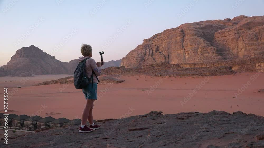 A tourist photographs the dawn in the desert. Young woman photographing sunrise using a smart phone A tourist photographs the dawn in the desert. Young woman photographing sunrise using a smart phone