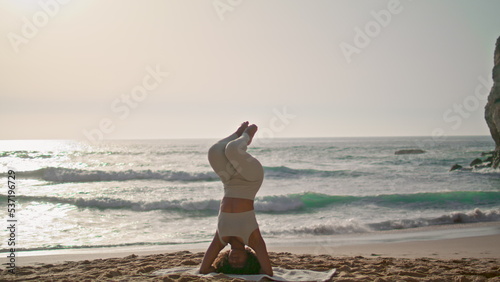 Girl practicing lotus headstand at sunrise Ursa beach. Lady exercising outdoor