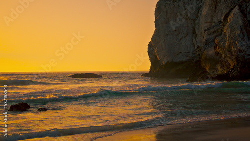Stone cliffs Ursa beach rising over water surface at sunrise. Calm ocean waves.