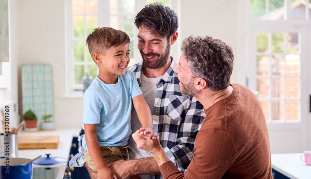 Same Sex Family With Two Dads Cooking In Kitchen With Son Sitting On ...