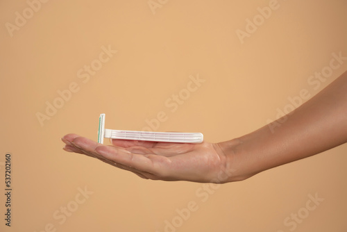 Womans hand hold razor on beige background beauty and healthcare concept