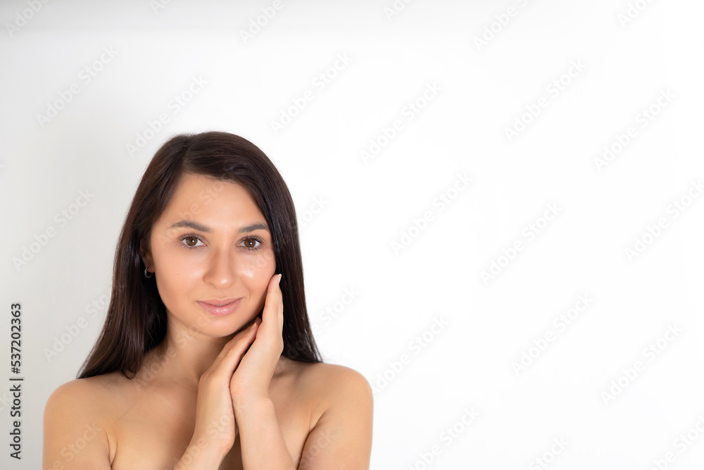 A natural portrait of a well-groomed young brunette woman with nude makeup. Gentle Beauty keeps her hands close to her face. White background place for text A natural portrait of a well-groomed young brunette woman with nude makeup. Gentle Beauty keeps her hands close to her face. White background place for text