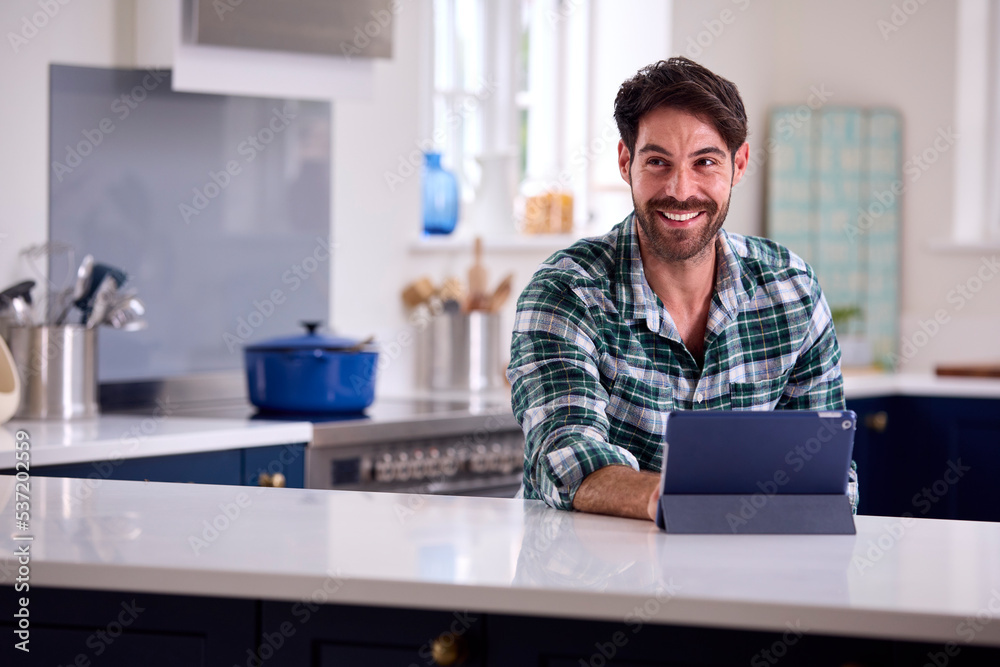 Man Using Digital Tablet In Kitchen To Work From Home Book Holiday Or Shop Man Using Digital Tablet In Kitchen To Work From Home Book Holiday Or Shop