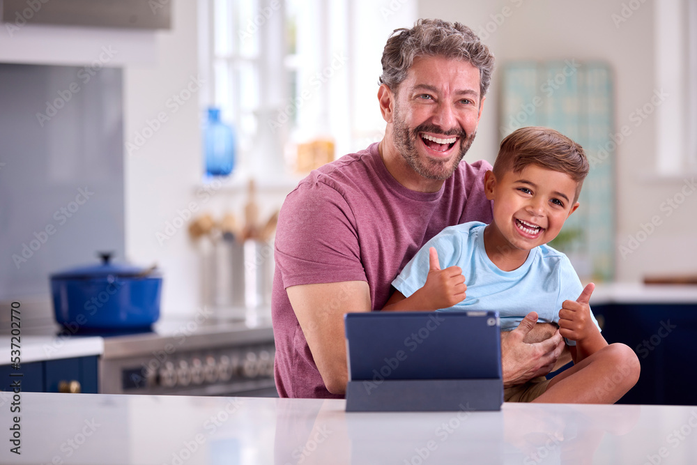 Mature Father At Home In Kitchen With Son Making Video Call On Digital Tablet Mature Father At Home In Kitchen With Son Making Video Call On Digital Tablet