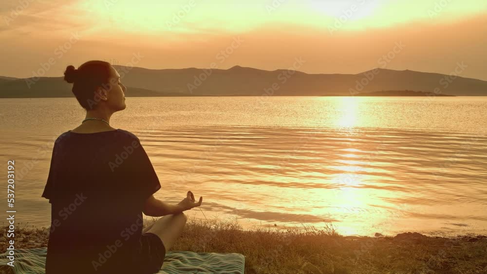 This video captures a woman sitting by the edge of a lake and meditating.