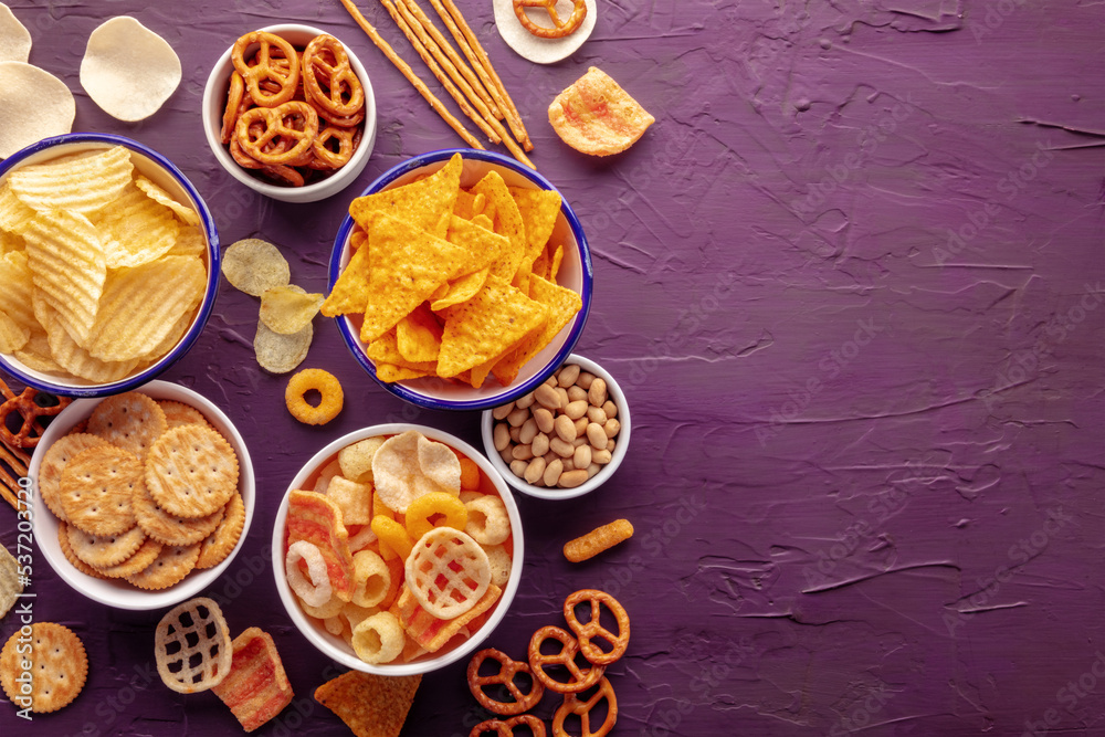 Salty snacks. Potato and tortilla chips, crackers and other appetizers in bowls, overhead flat lay shot with copy space. Party food background