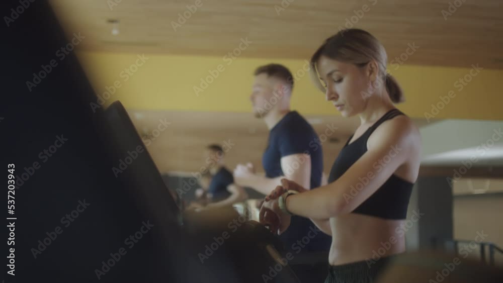 Waist up shot of beautiful blonde woman walking on treadmill and checking smartwatch while training in gym Waist up shot of beautiful blonde woman walking on treadmill and checking smartwatch while training in gym