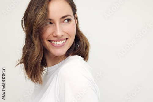 Portrait of beautiful naturally brunette woman, smiling and looking cute to the right. Close-up portrait of caucasian female girl isolated on white background.	