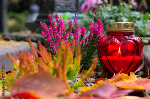 A red heart-shaped candle on a grave  in a cemetery on an autumn day. All Saints Day. Copy space, shallow depth of field.