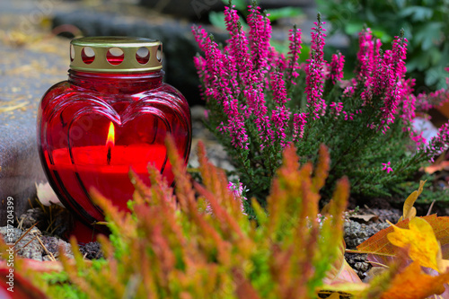 A red heart-shaped candle on a grave  in a cemetery on an autumn day. All Saints Day. Copy space, shallow depth of field. photo