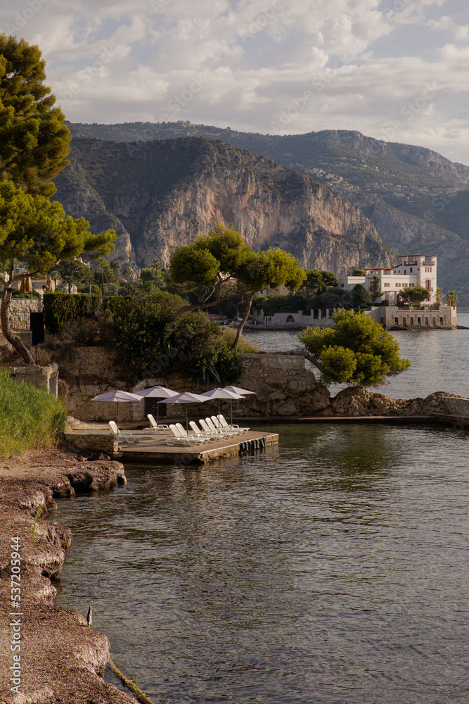 Fototapeta premium View of the sea coast against the background of the mountains. Dawn over the picturesque coast. Sun loungers and umbrellas waiting for holidaymakers. Ideal place to relax