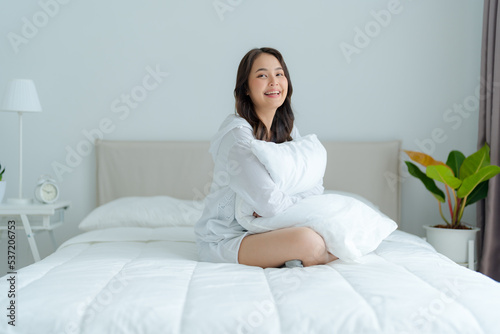 A beautiful woman sitting on a pillow in her bedroom, smiling, laughing happily.