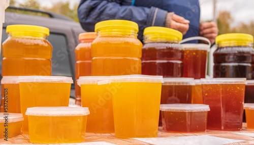 On counter is honey, packed in plastic containers of different sizes. Autumn agricultural fair. photo