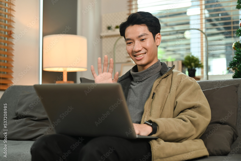 Satisfied man wearing warm sweater having a video call with friends or family on laptop while sitting on couch at home Satisfied man wearing warm sweater having a video call with friends or family on laptop while sitting on couch at home