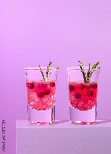 cocktail with cranberries with ice in glasses on a lilac background. Two shots with berries and rosemary, copy space