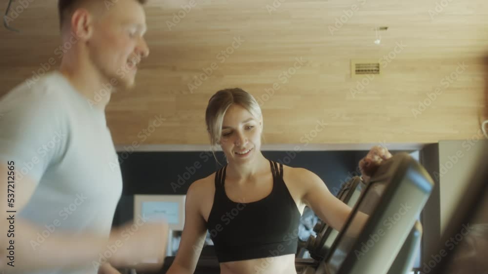 Cheerful female trainer speaking with man as he running on treadmill during gym workout Cheerful female trainer speaking with man as he running on treadmill during gym workout